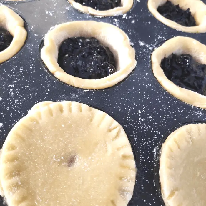 placing pastry lids on top of blackcurrant pies mr kipling style