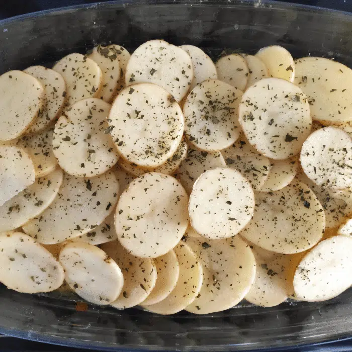 thinly sliced potatoes on top of sausages, lentils and veg
