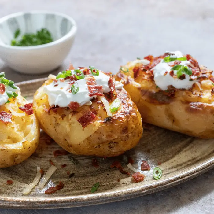 slow cooker baked potatoes topped with sour cream, bacon and spring onion