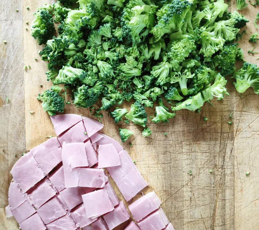 chopped broccoli heads and chopped ham on chopping board