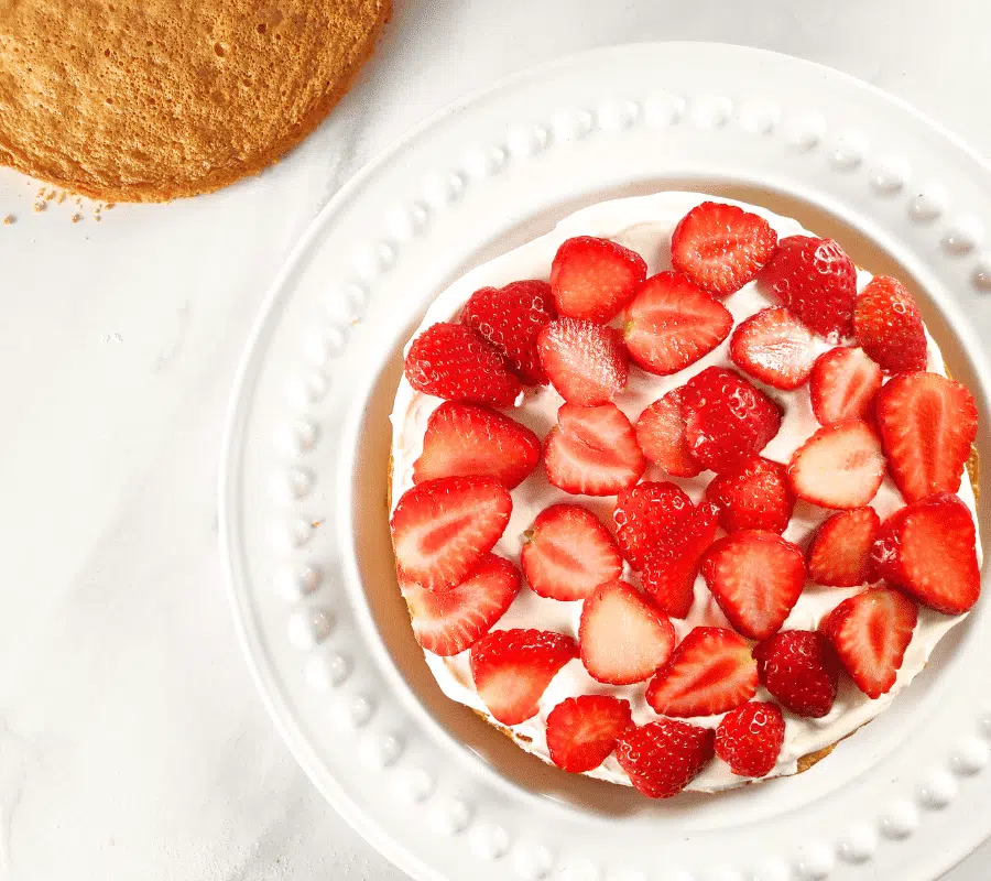 cream and sliced strawberries on top of sponge cake