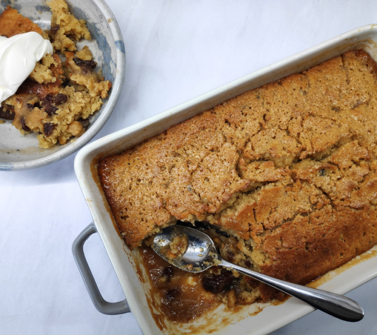 rum and raisin sponge pudding in an oven proof dish and one scoop of it in a bowl topped with cream