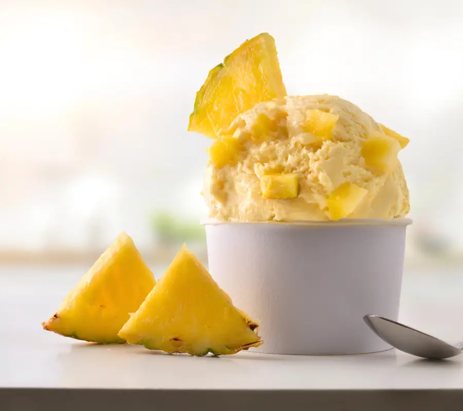 hawaiian pineapple ice cream in a white pot with pieces of fresh pineapple
