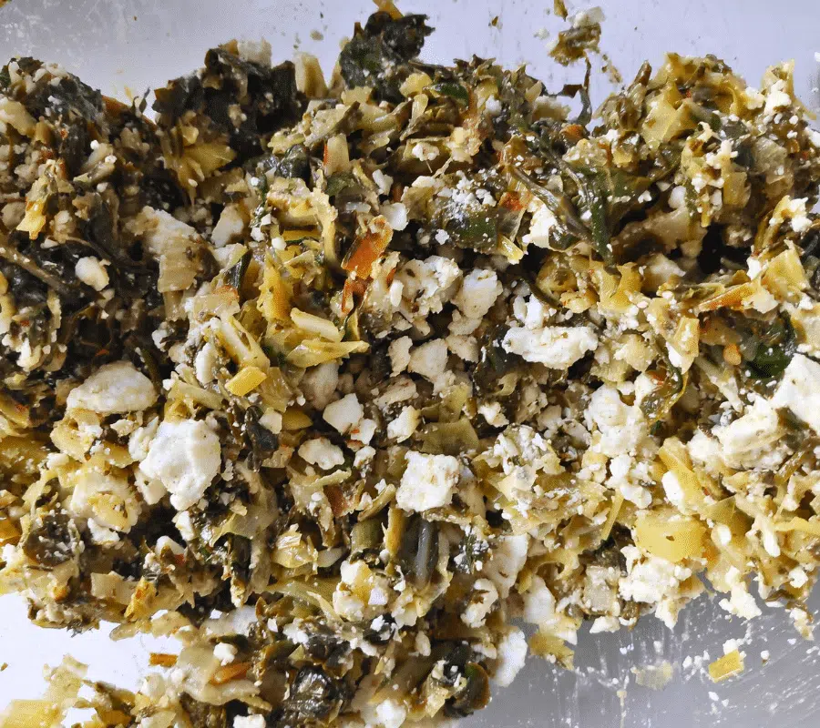 Feta cheese added to chard pie filling in a bowl