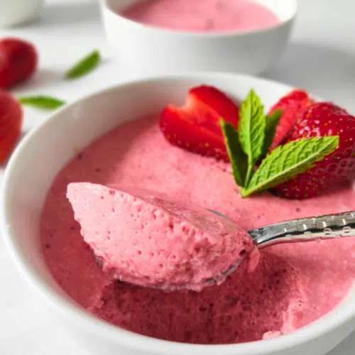 strawberry mousse in a white pot topped with sliced of strawberries and a sprig of mint uk