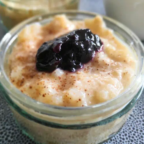 protein rice pudding with a dollop of jam on top in a clear glass ramekins dish
