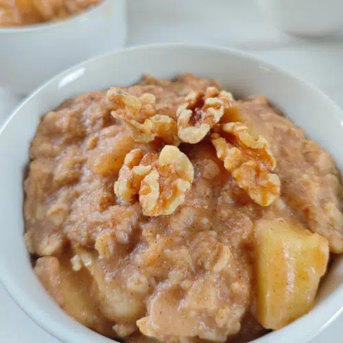 a small white bowl with overnight oats apple and cinnamon top with a few walnuts