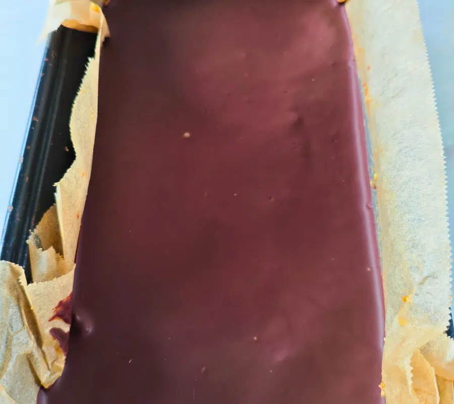 freshly made date flapjack topped with dark chocolate in a loaf tin lined with baking paper