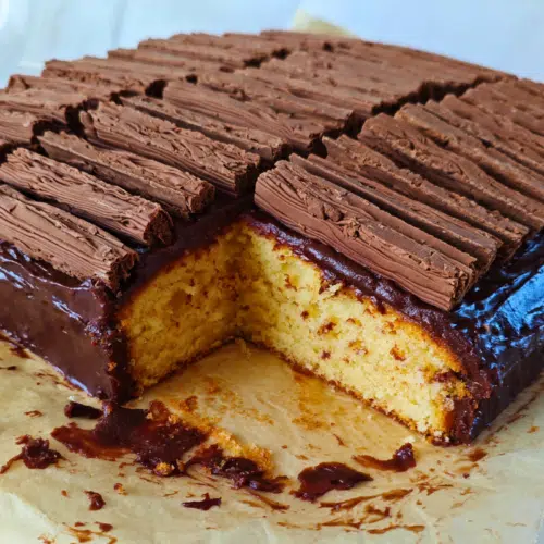 cadburys flake traybake with a corner piece taken out showing a plain sponge, chocolate custard topping topped with cadburys flakes