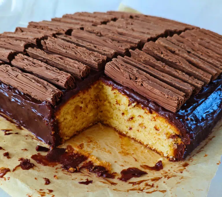 cadburys flake traybake with a corner piece taken out showing a plain sponge, chocolate custard topping topped with cadburys flakes