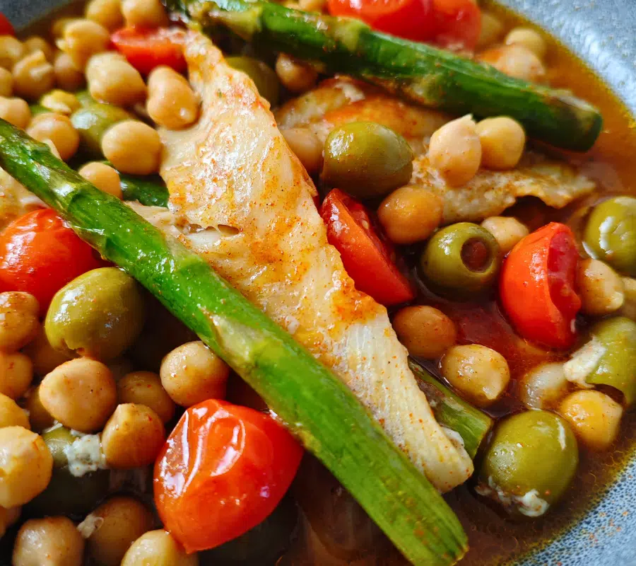 Alaska pollock fish in a bowl with chickpeas, asparagus, cherry tomatoes and olives