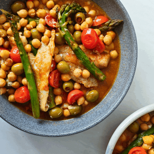 pollock fish in a bowl with chickpeas, asparagus, cherry tomatoes and olives