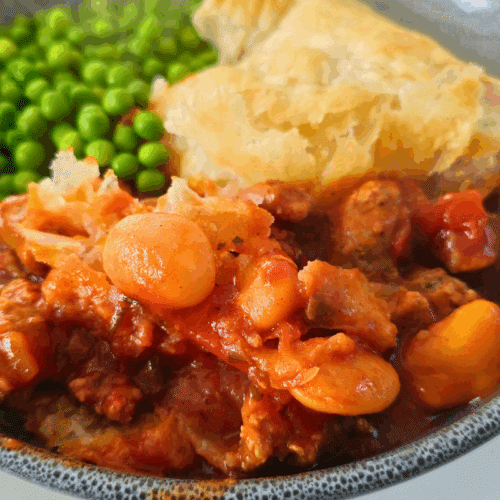 sausage abd butterbean puff pastry pie in a bowl with peas