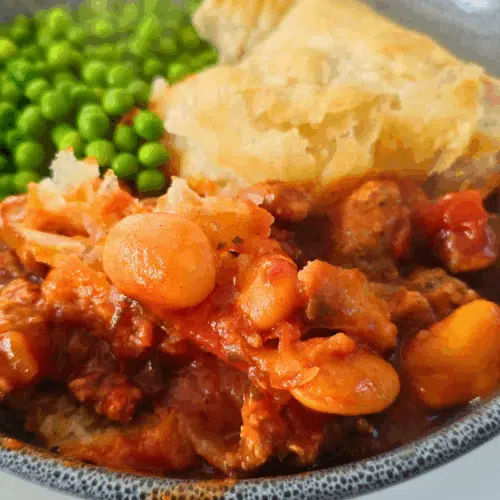sausage abd butterbean puff pastry pie in a bowl with peas