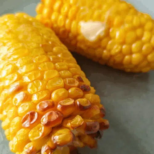 two corn on the cobs on a plate topped with a knob of butter