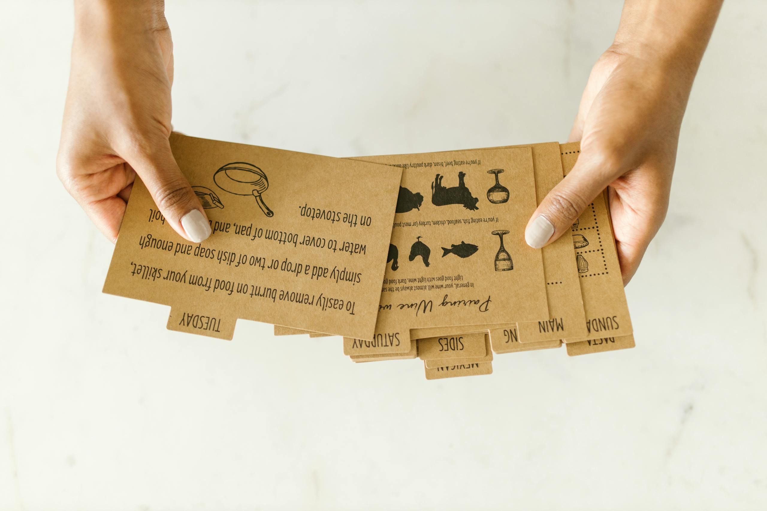 Brown kraft paper recipe cards held by hand on light background.