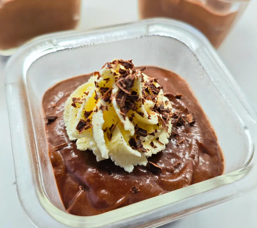 Dark chocolate mousse in a clear square glass dish topped with a swirl of double cream