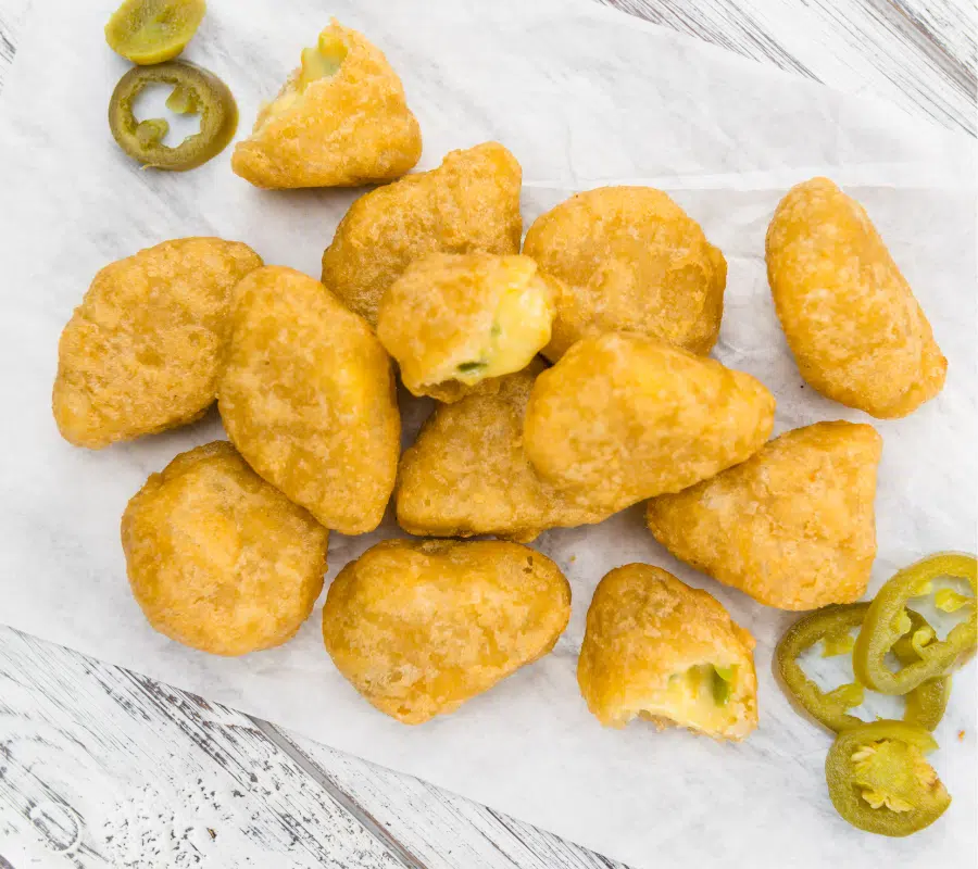 cheese chili nuggets on white greaseproof paper on a white table with scattered jalapenos