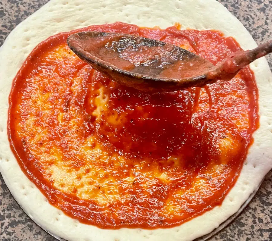 passata pizza sauce being spread on a pizza dough